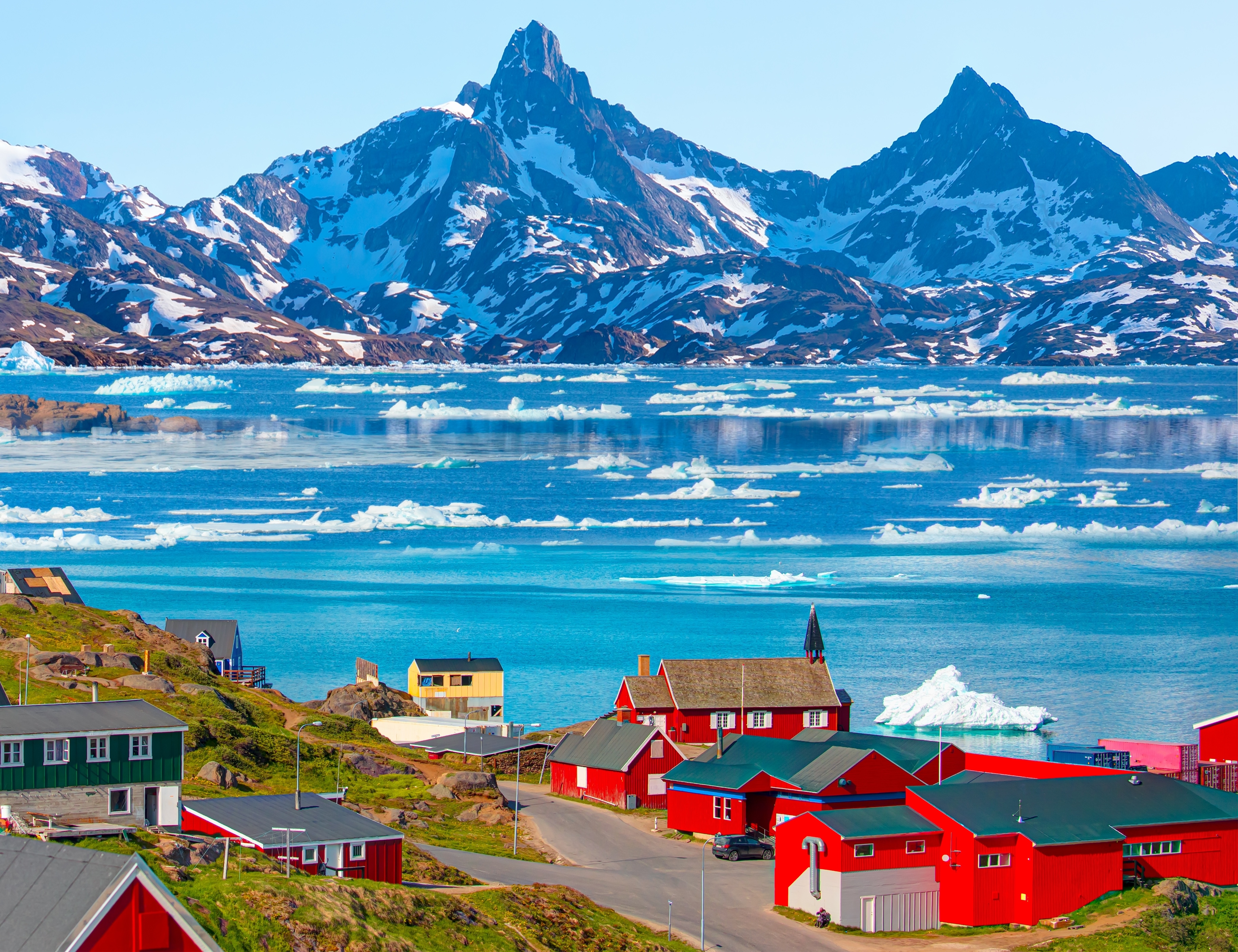 Colorful houses in Tasiilaq, Greenland, overlooking icy coastal waters and snow-covered mountains.