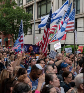 Jewish and pro-Israel activists protest in New York City while holding Israeli and American flags.