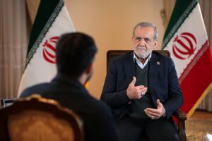 Iranian President Masoud Pezeshkian speaks during an interview with Iranian flags behind him.