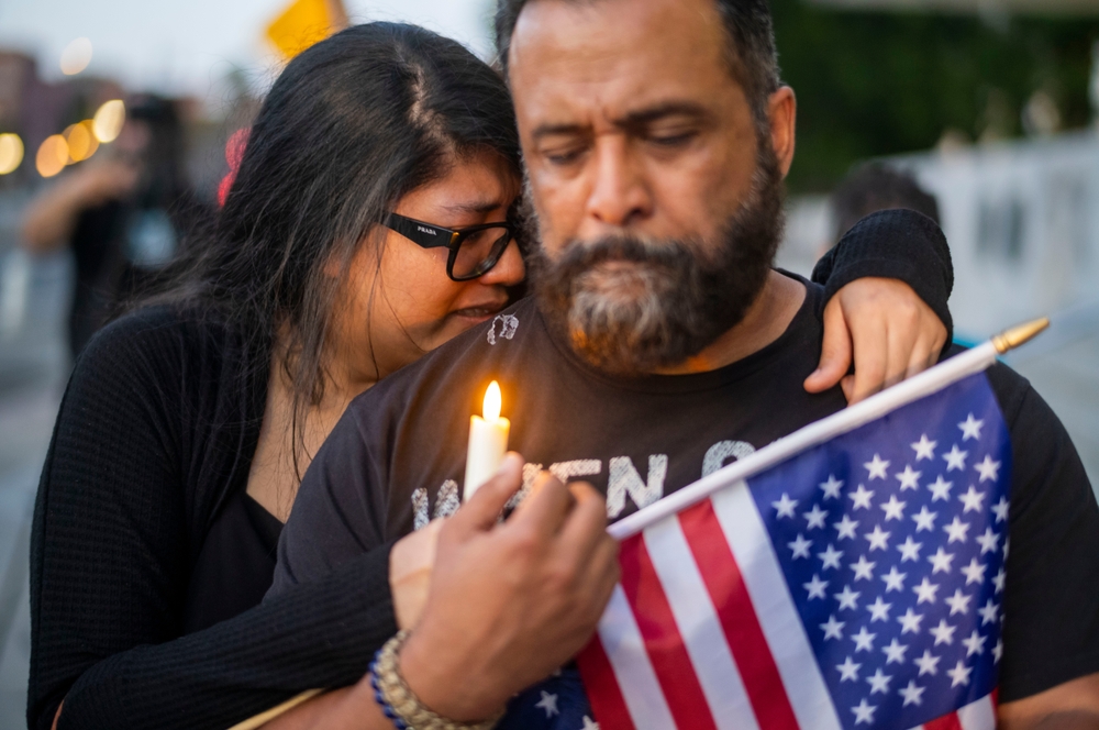 two people with candle, crying, and american flag at vigil for charlie kirk