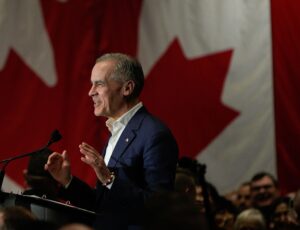 Canadian Prime Minister Mark Carney speaking at a podium in front of a large Canadian flag.