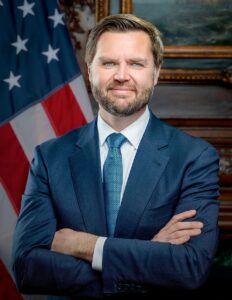 Official portrait of J.D. Vance in a blue suit with an American flag behind him.