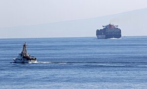 A U.S. Coast Guard cutter transits the Strait of Hormuz near a large cargo ship.