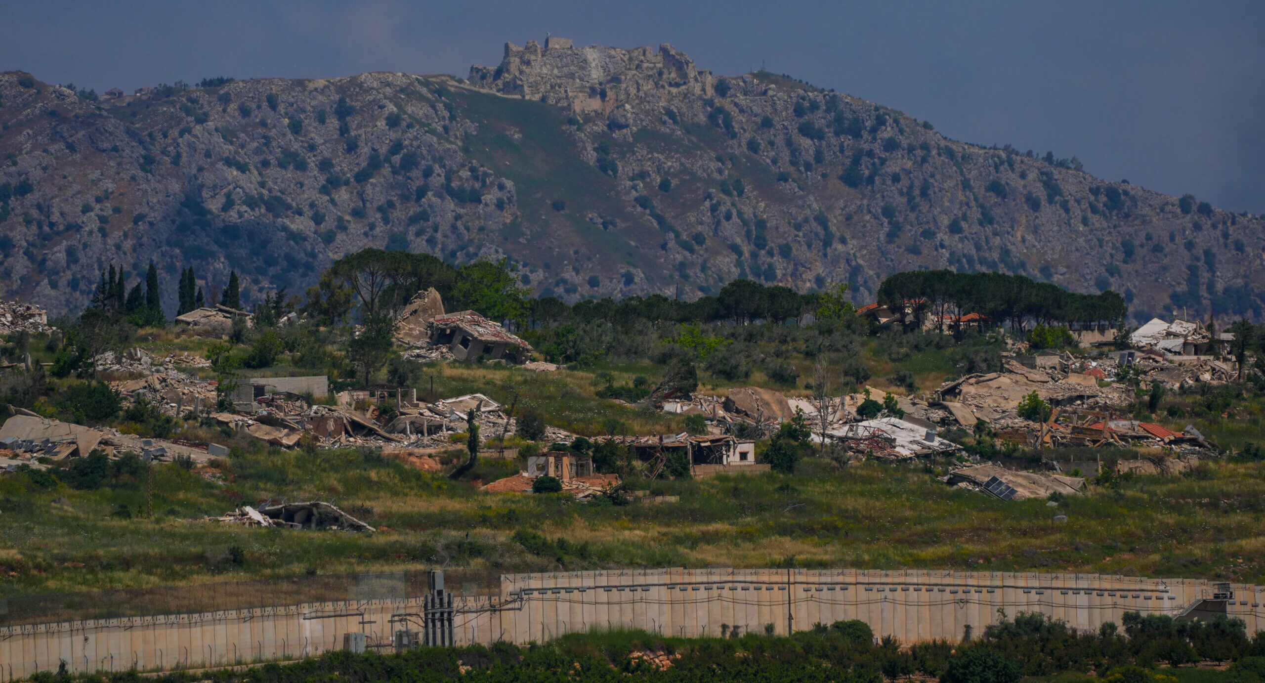Destroyed buildings and open terrain near a mountainous border area.