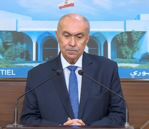 Lebanese lawmaker Fouad Makhzoumi speaking at a podium with the Lebanese flag behind him.