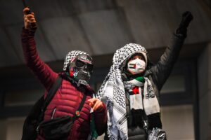 Masked anti-Israel protesters wearing keffiyehs and raising their fists.