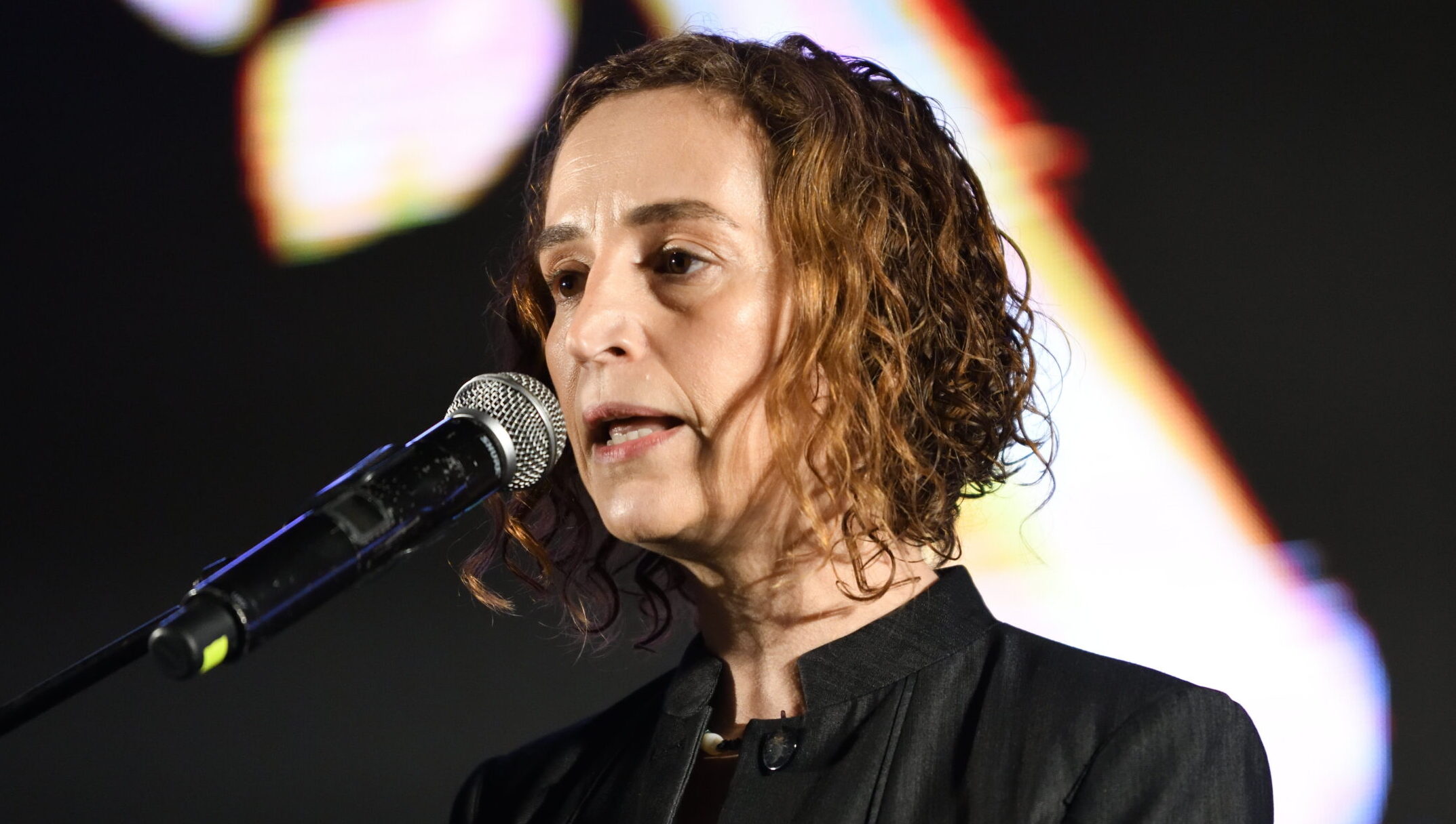 Eynat Guez speaking into a microphone at a rally in Tel Aviv.