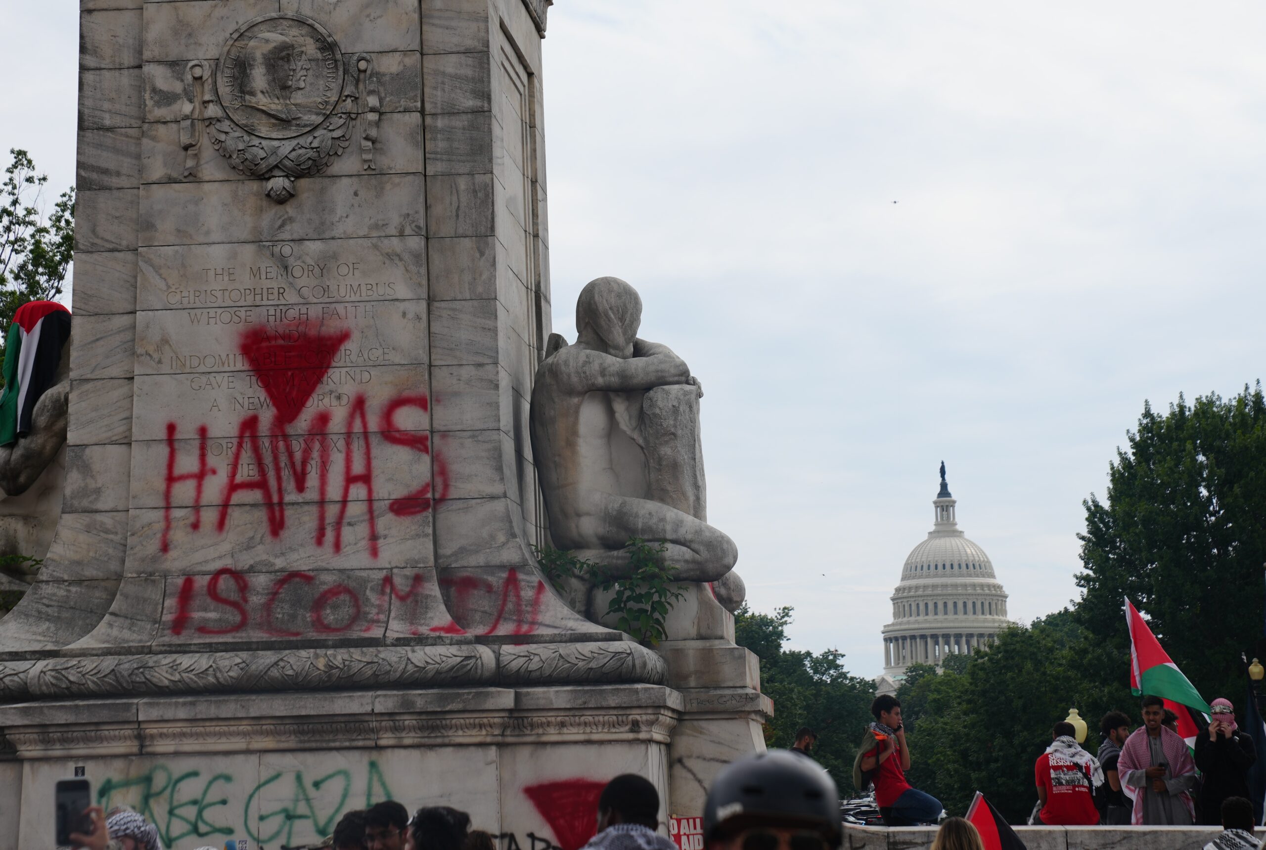 Pro-Palestinian demonstrators near a vandalized monument in Washington, D.C., with the U.S. Capitol visible in the background.