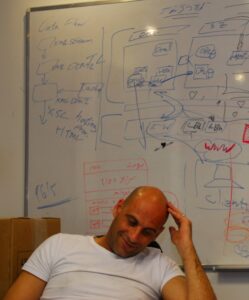 Israeli startup founder Chen Amishay sitting in an office with a whiteboard behind him.