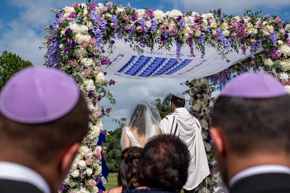 jewish couple under chuppah adorned with flowers