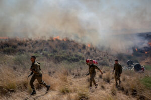 IDF soldiers walking near a fire caused by kites flown from Gaza near Kibbutz Be’eri.