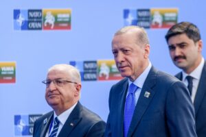 Turkish officials standing in front of NATO and summit signs.