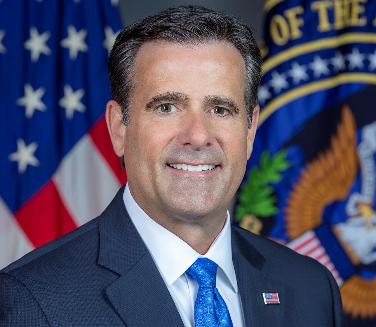 Portrait of a senior U.S. intelligence official in front of American flags.