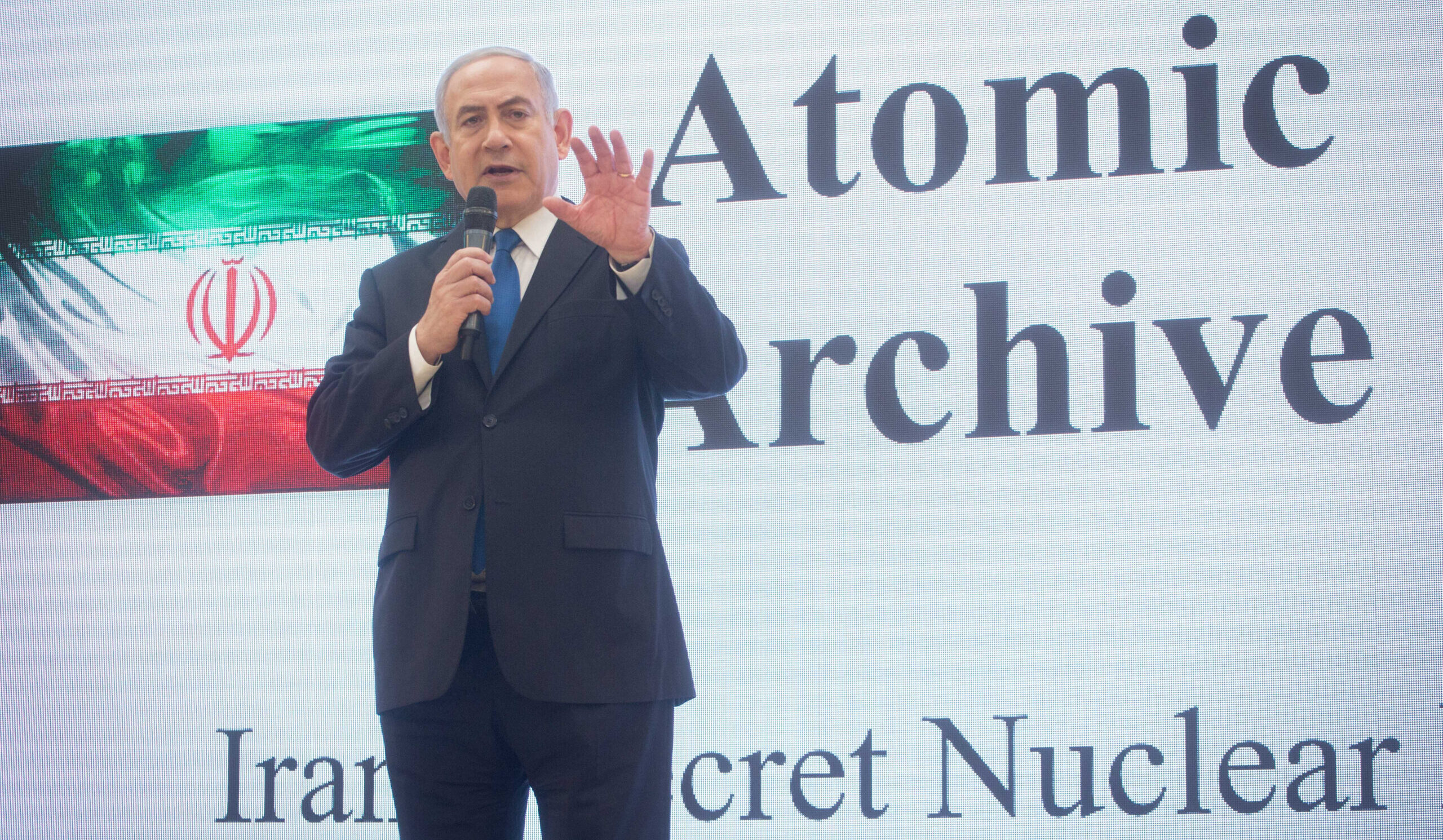 Prime Minister Benjamin Netanyahu speaks beside an image of the Iranian flag and text about Iran’s nuclear archive.