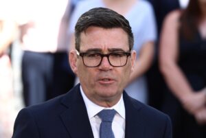 UK Prime Minister Andy Burnham speaking outdoors in a dark suit and glasses.