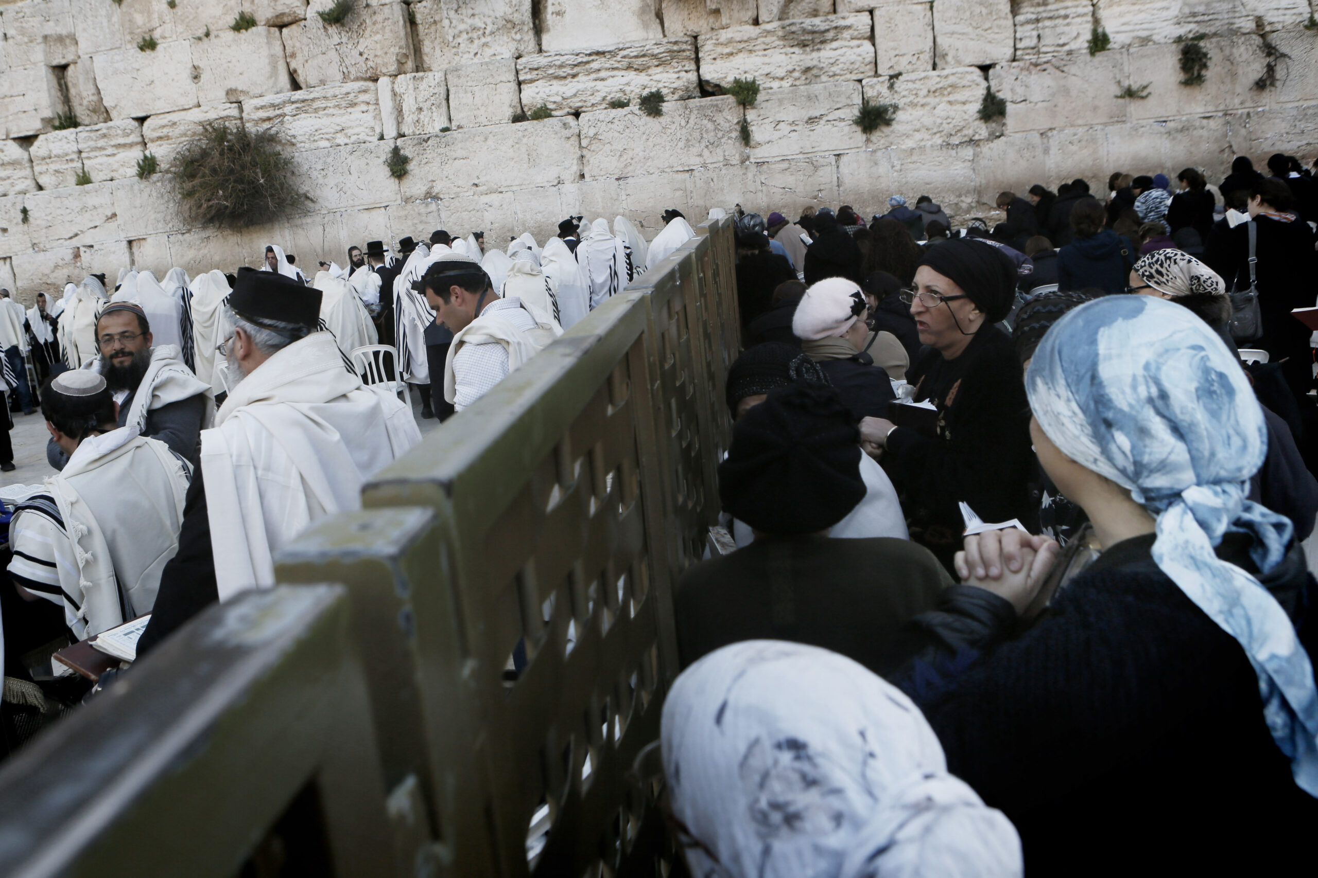 Orthodox Jewish women look over the divider at the Western Wall while men pray.