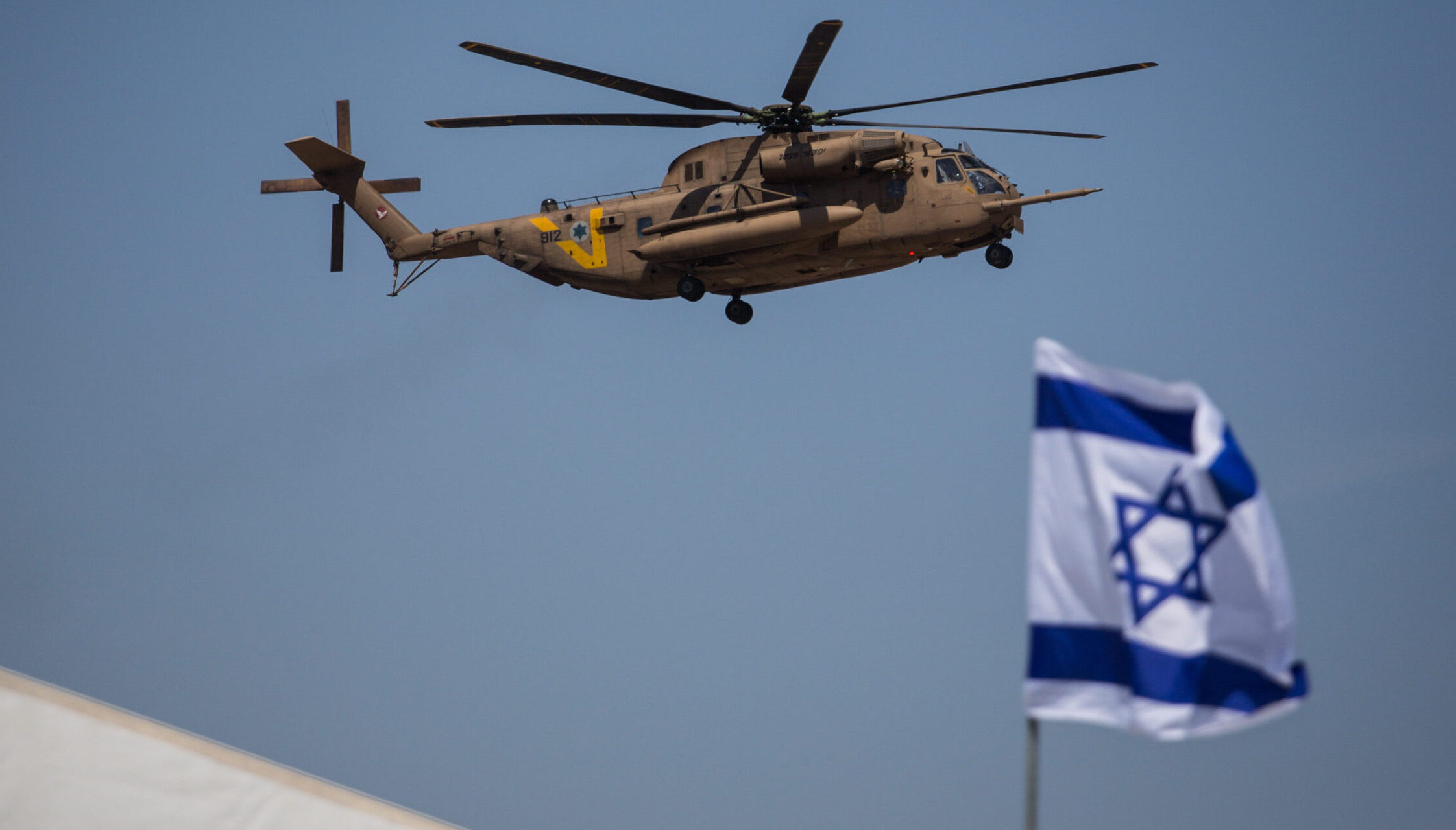 A US Army helicopter flies over Ben Gurion Airport beside an Israeli flag.