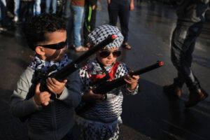 Palestinian children carrying toy guns during a military parade in the Qalandiya refugee camp.