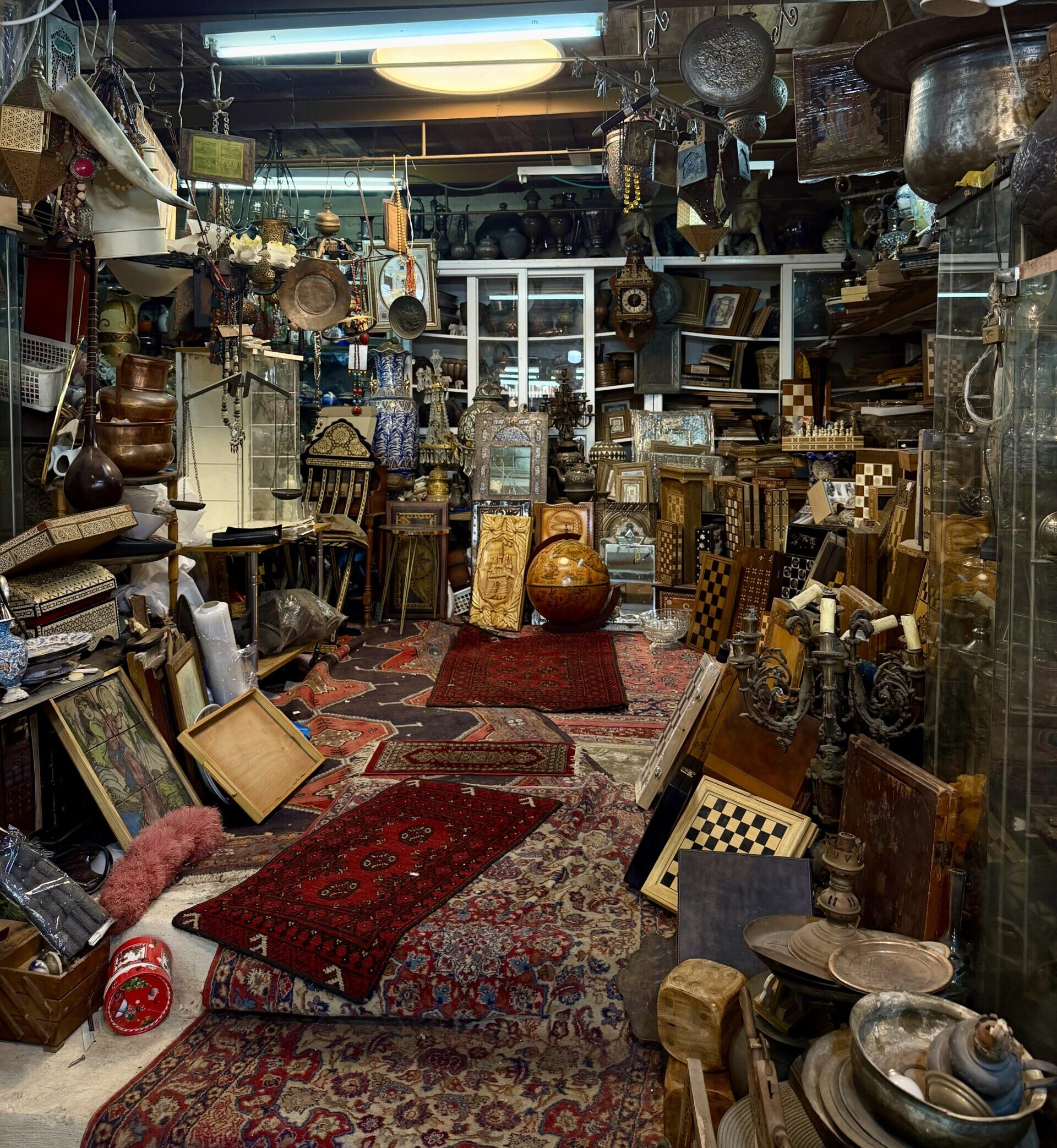 Interior of a shop in the Jaffa Flea Market filled with Persian rugs, antiques, artwork, and decorative objects.