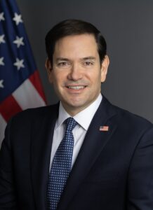 U.S. Secretary of State Marco Rubio posing for an official portrait with an American flag behind him.