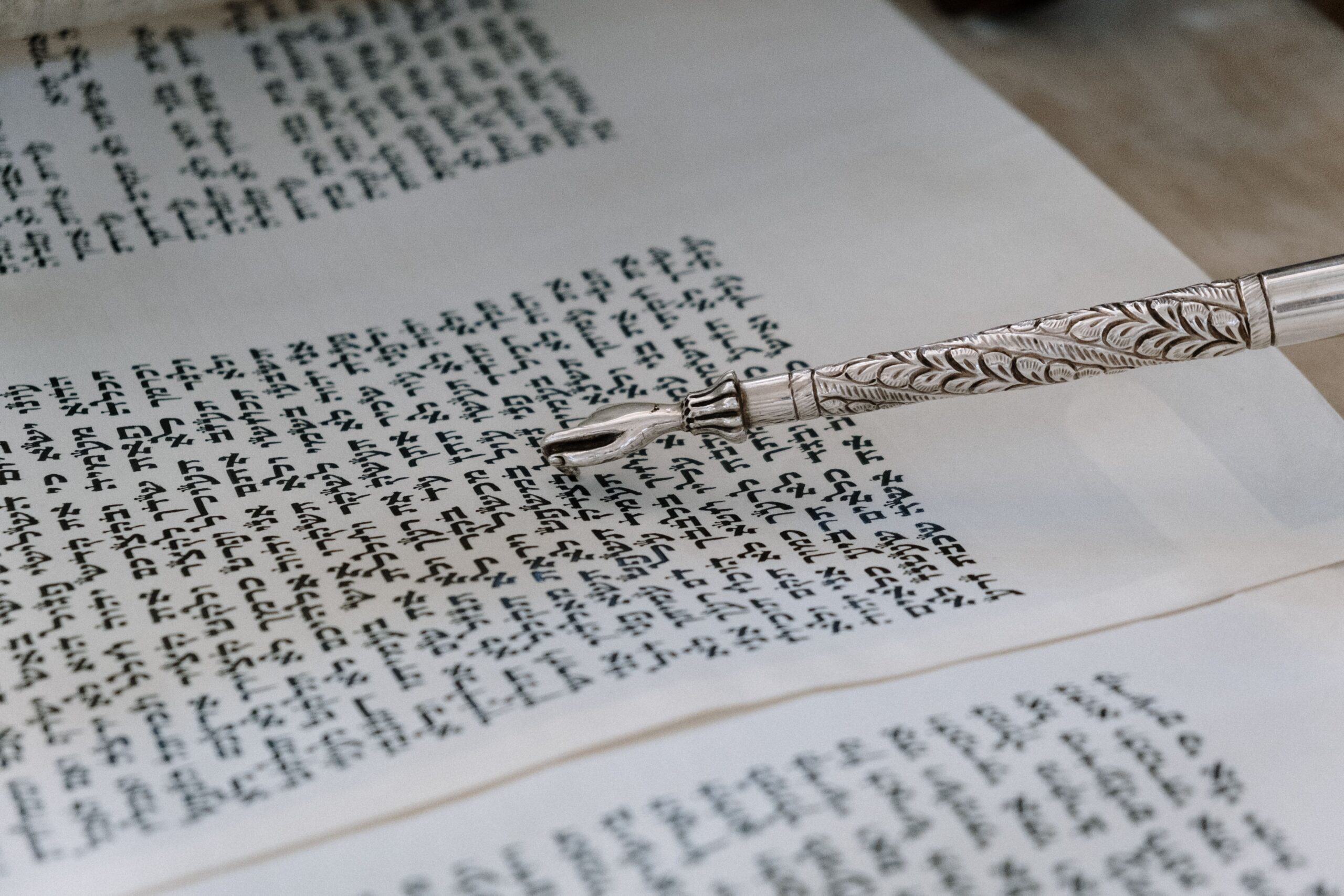 An open Torah scroll with a "yad" pointing at the Hebrew Letters