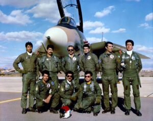 Iranian fighter pilots standing and kneeling in front of a military aircraft.