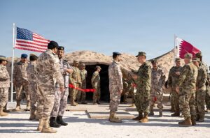 U.S. and Qatari military personnel stand near American and Qatari flags at Al Udeid Air Base.