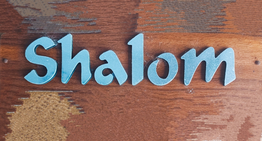 letters of the word Shalom painted in blue on wood background