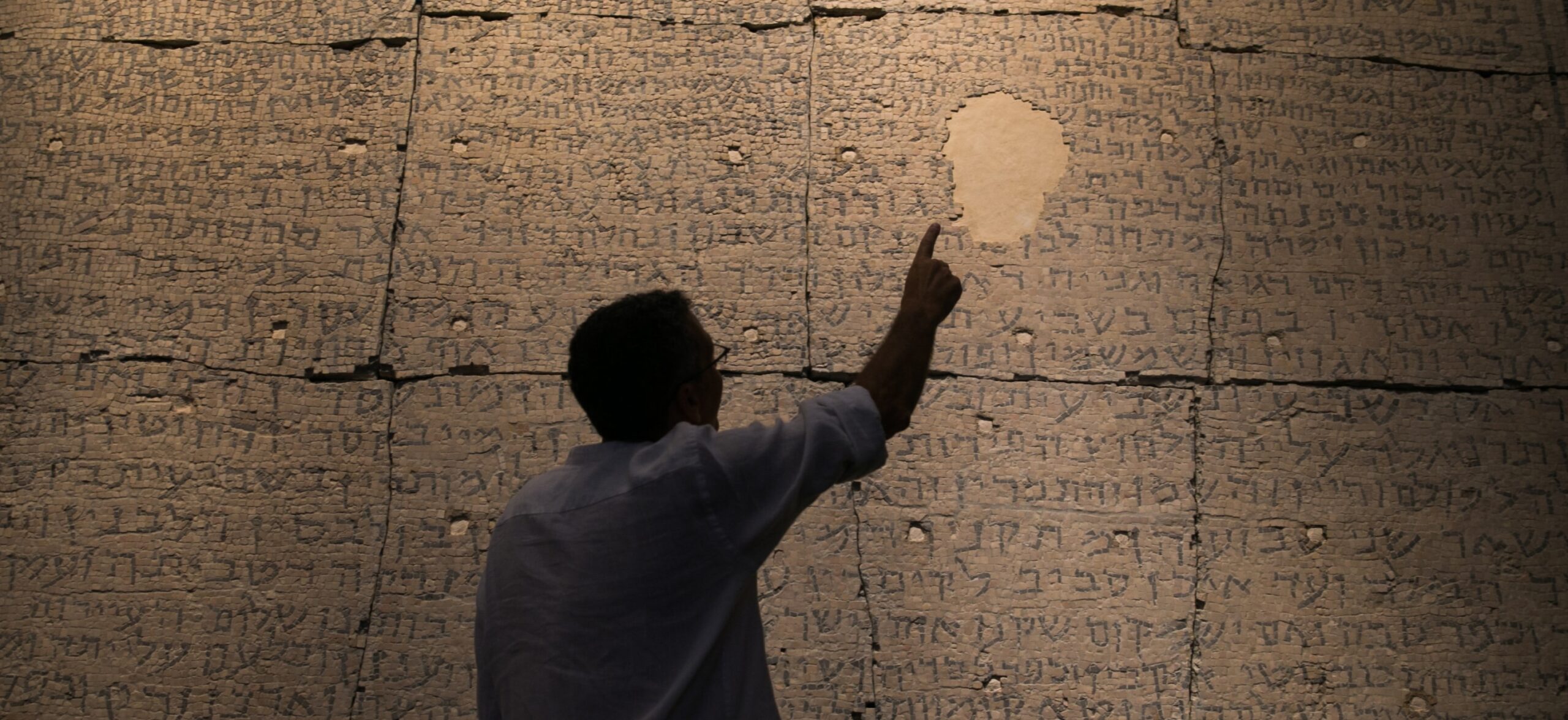 A visitor points toward an ancient Hebrew and Aramaic inscription at the Israel Museum in Jerusalem.