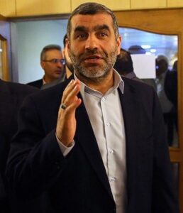Ali Nikzad speaks while raising his hand indoors.