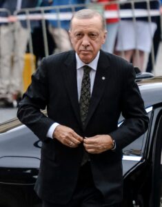 Recep Tayyip Erdogan wearing a dark suit beside a vehicle