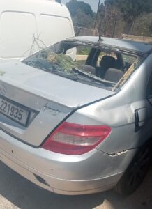 Rear view of a damaged silver vehicle with a shattered back window and debris inside.