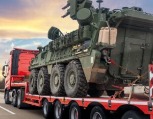 A U.S. armored military vehicle transported on a trailer during a convoy in Eastern Europe.