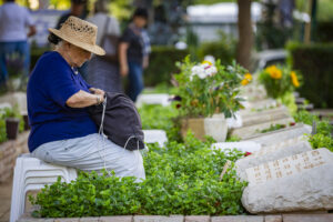 Woman sitting beside graves of fallen Israeli soldiers at a military cemetery in Haifa.