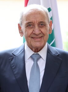 Nabih Berri, Speaker of the Lebanese Parliament, standing in front of a Lebanese flag.