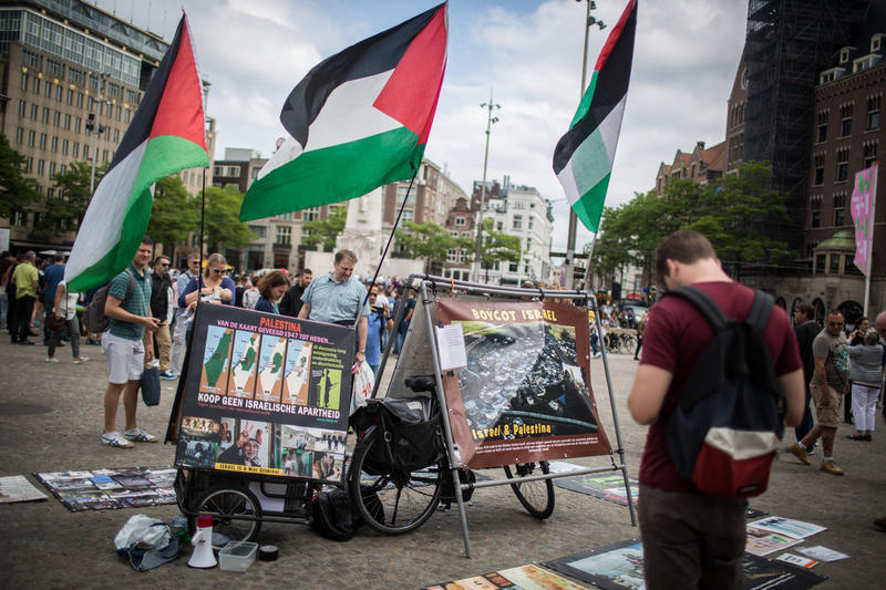 Israeli tourists look at a BDS stand with photos and Palestinian flags, calling to 'Free Palestine,' at Dam Square in central Amterdam, Holland