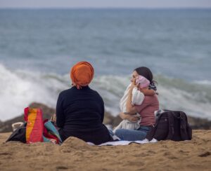 People sitting on the beach in Nahariya as waves hit the shore